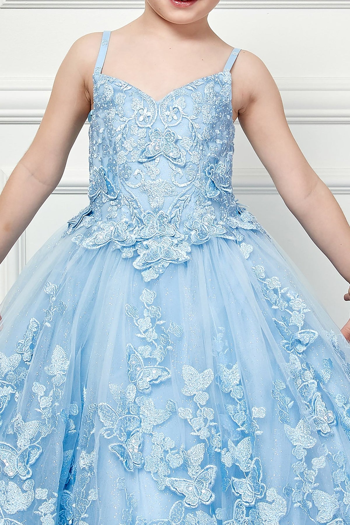 Zoomed front view of a blue kids mini quinceanera mini quince dress highlighting butterfly floral appliques, gem accents, and glitter tulle skirt.