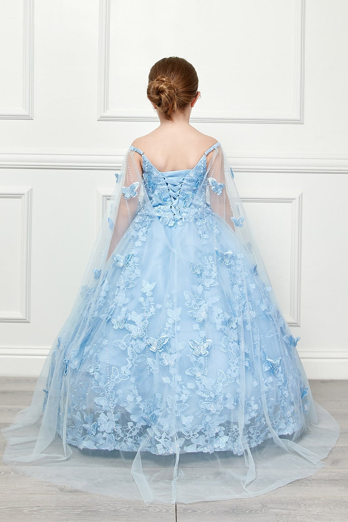 Back view of a blue kids mini quinceanera mini quince dress with lace-up corset, oversized bow, butterfly floral appliques, and detachable cape.