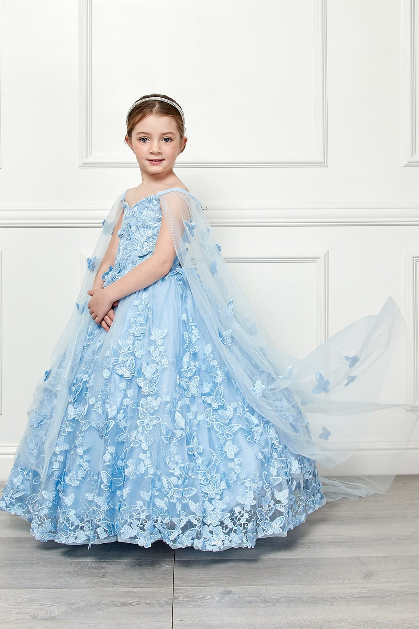 Side view of a blue kids mini quinceanera mini quince dress with butterfly floral appliques, off-shoulder neckline, and detachable cape.