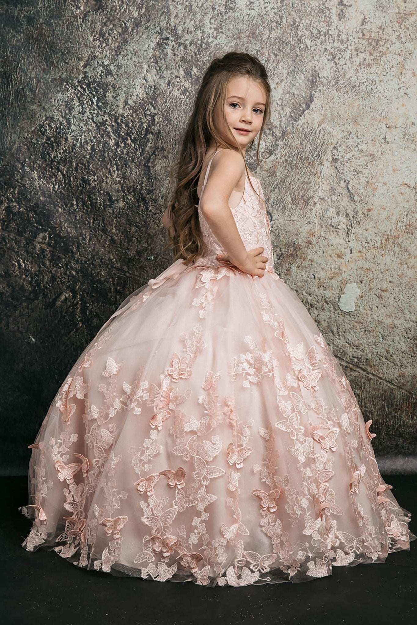 Side view of a blush kids mini quinceanera dress with butterfly floral appliques, off-shoulder neckline, and flowing cape