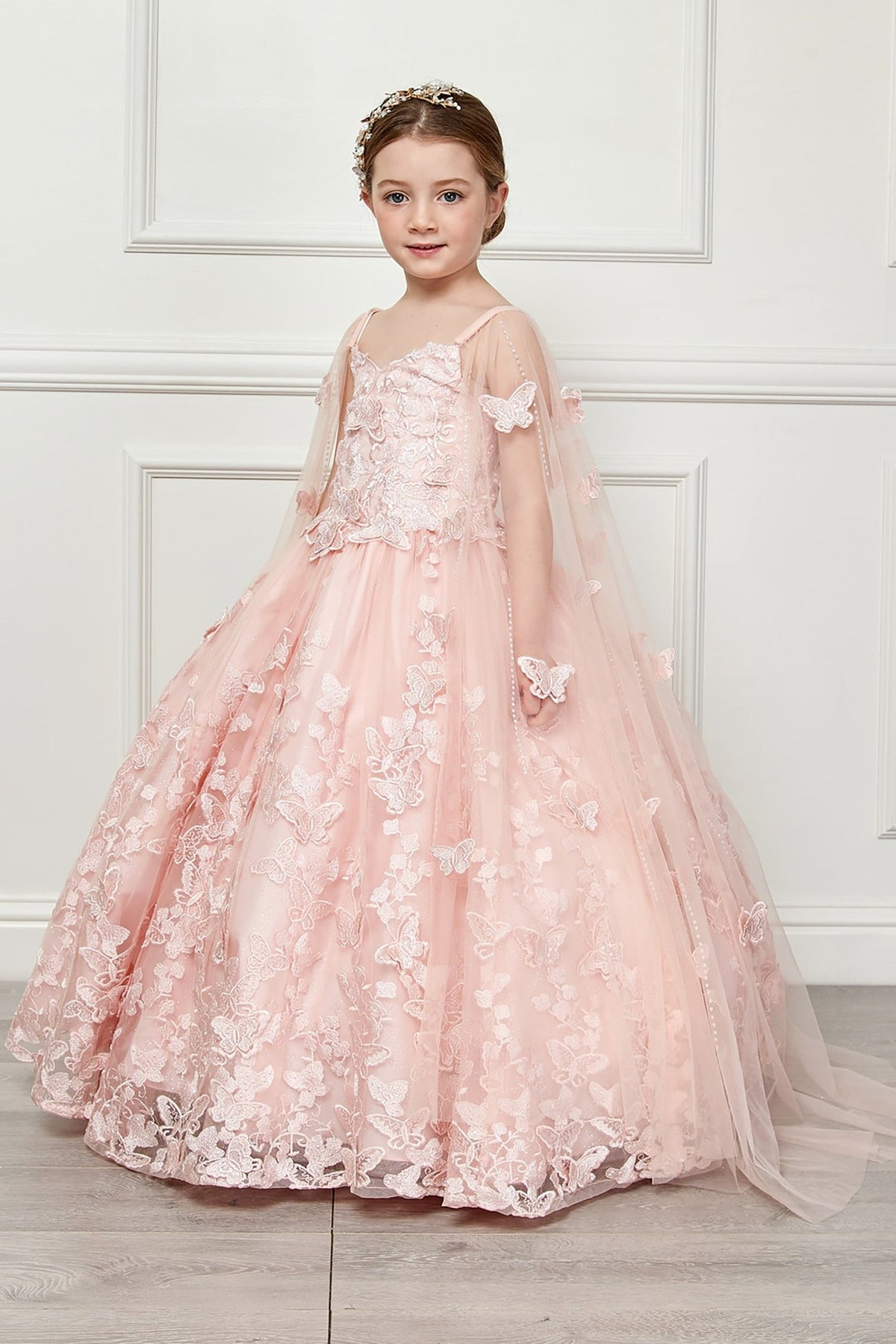 Side view of a blush kids mini quinceanera mini quince dress with butterfly floral appliques, off-shoulder neckline, and flowing cape.
