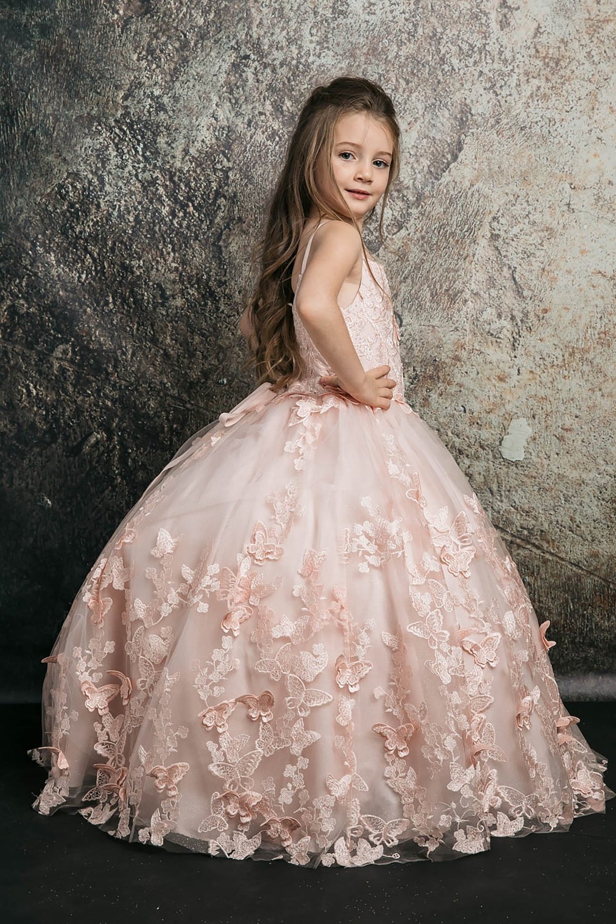 Side view of a blush kids mini quinceanera mini quince dress with butterfly floral appliques, off-shoulder neckline, and flowing cape.