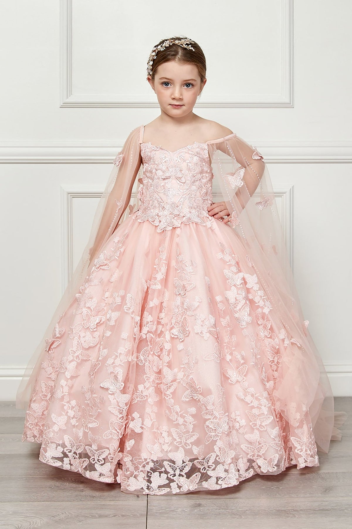 Front view of a blush kids mini quinceanera mini quince dress with 3D butterfly floral appliques, off-shoulder neckline, and flowing cape.