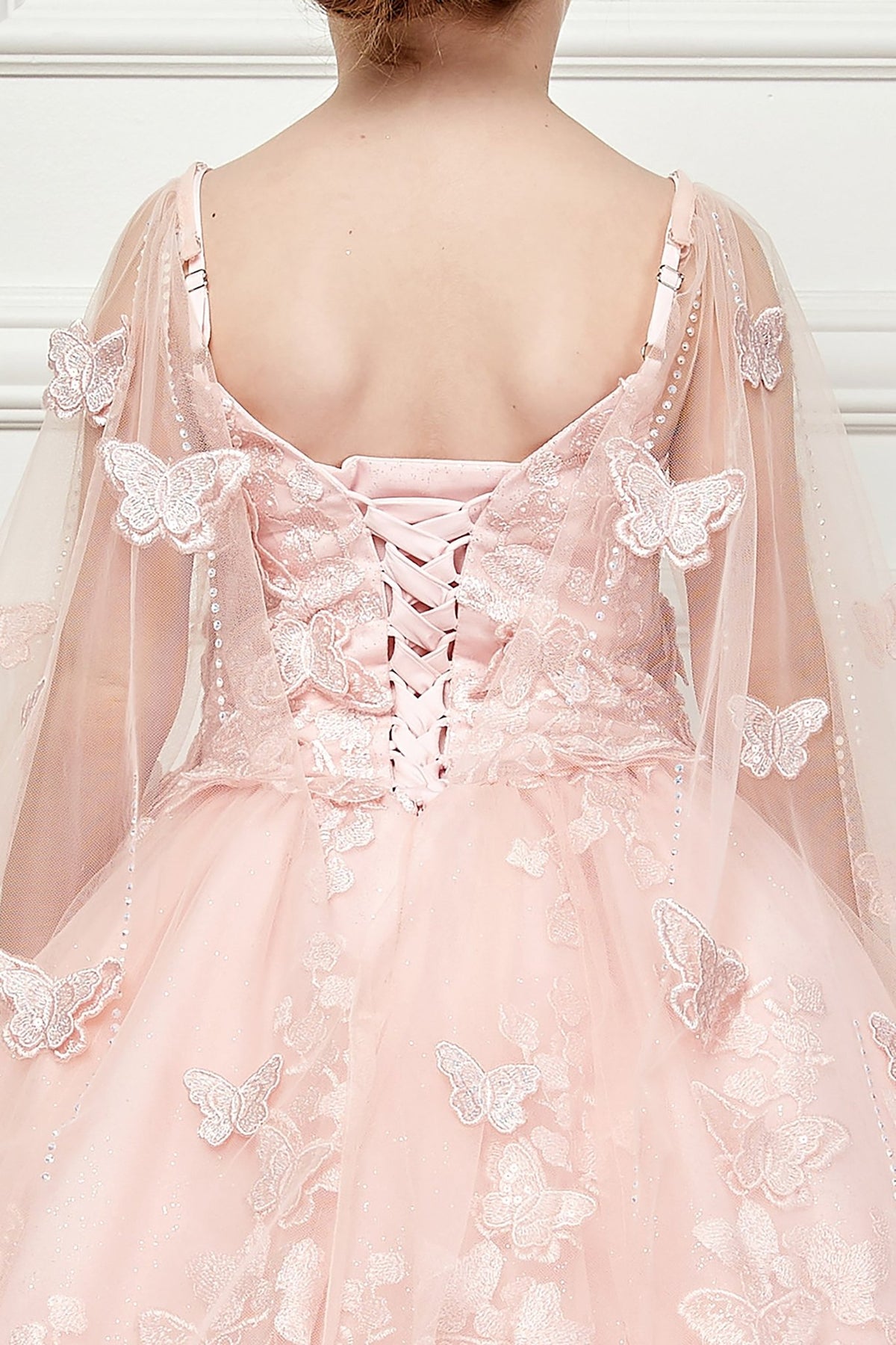 Back view of a blush kids mini quinceanera mini quince dress with lace-up corset, oversized bow, butterfly floral appliques, and detachable cape.