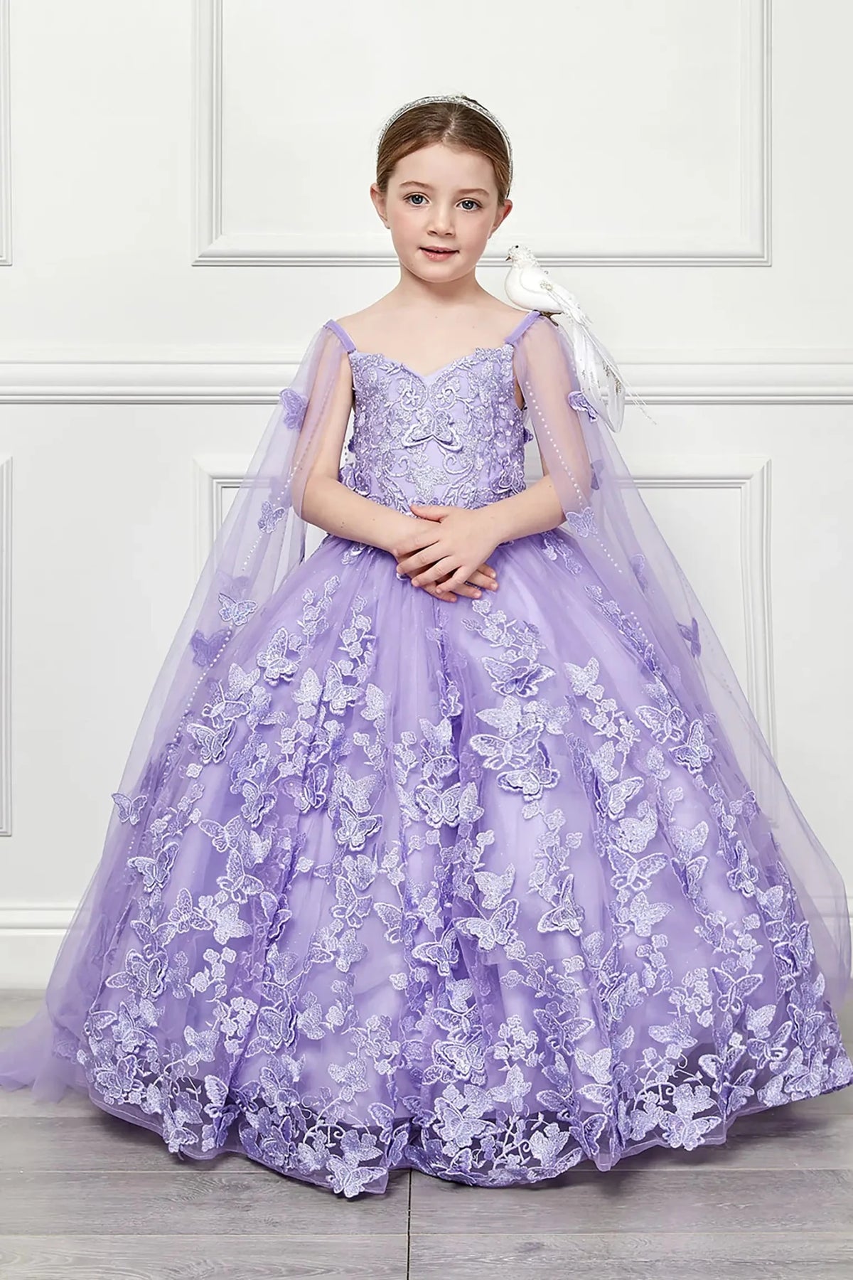 Front view of a lilac kids mini quinceanera mini quince dress with 3D butterfly floral appliques, off-shoulder neckline, and flowing cape.