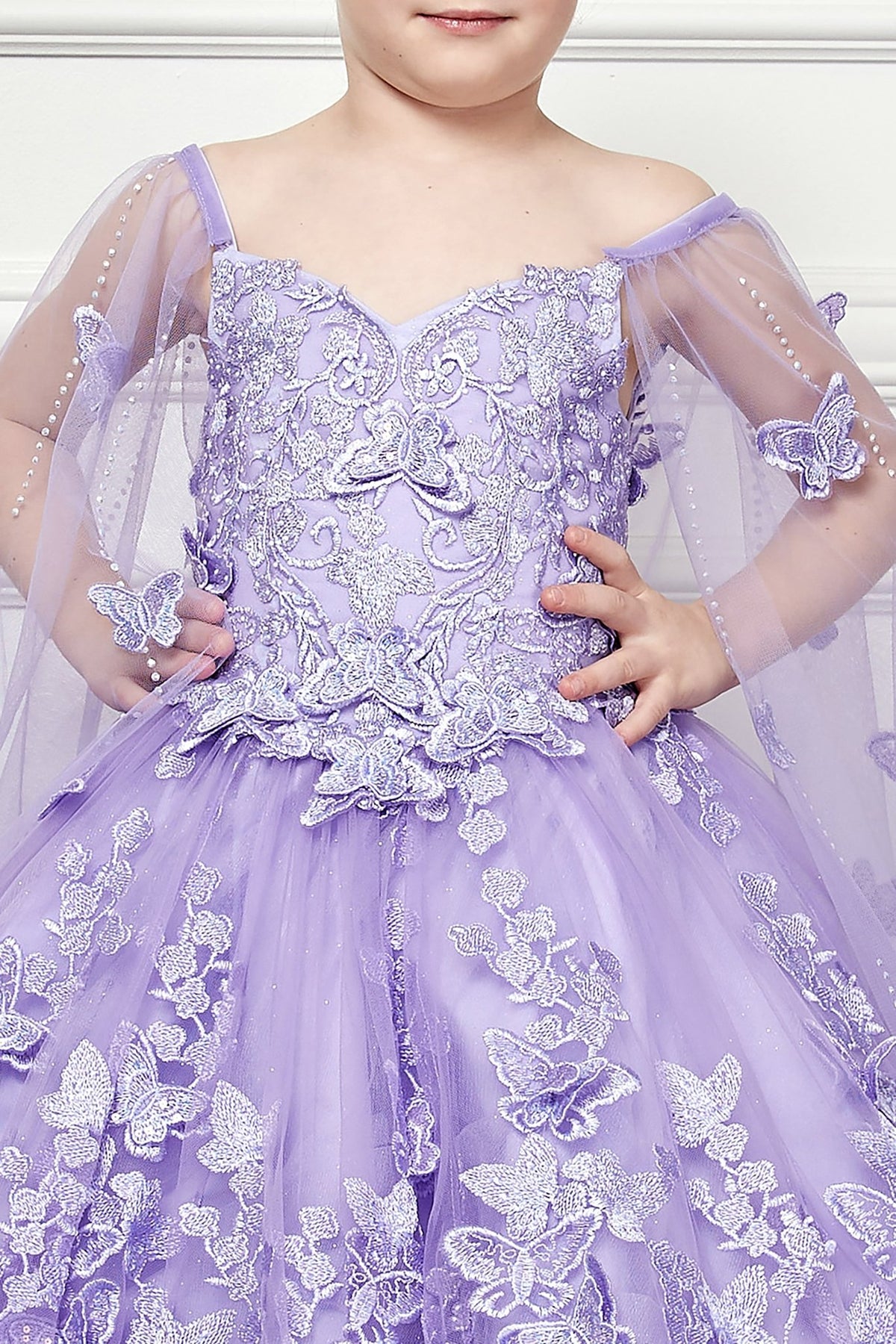 Zoomed front view of a lilac kids mini quinceanera mini quince dress highlighting butterfly floral appliques, gem accents, and glitter tulle skirt.