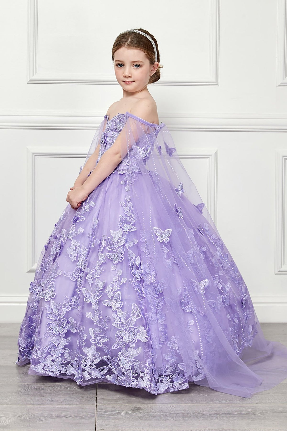 Side view of a lilac kids mini quinceanera mini quince dress with butterfly floral appliques, off-shoulder neckline, and flowing cape.