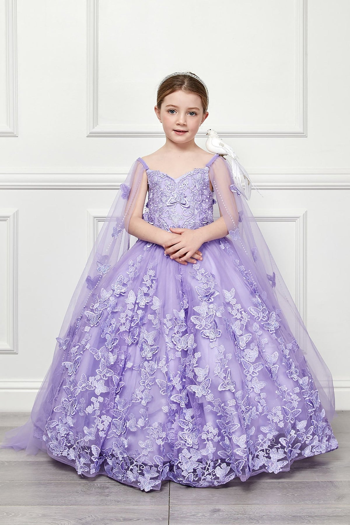 Front view of a lilac kids mini quinceanera mini quince dress with 3D butterfly floral appliques, off-shoulder neckline, and flowing cape.
