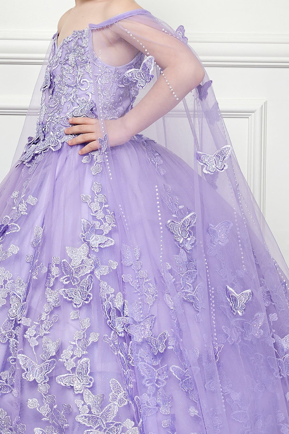 Side close-up of a lilac kids mini quinceanera mini quince dress showing butterfly floral appliques, puffed sleeve detail, and glitter tulle fabric.