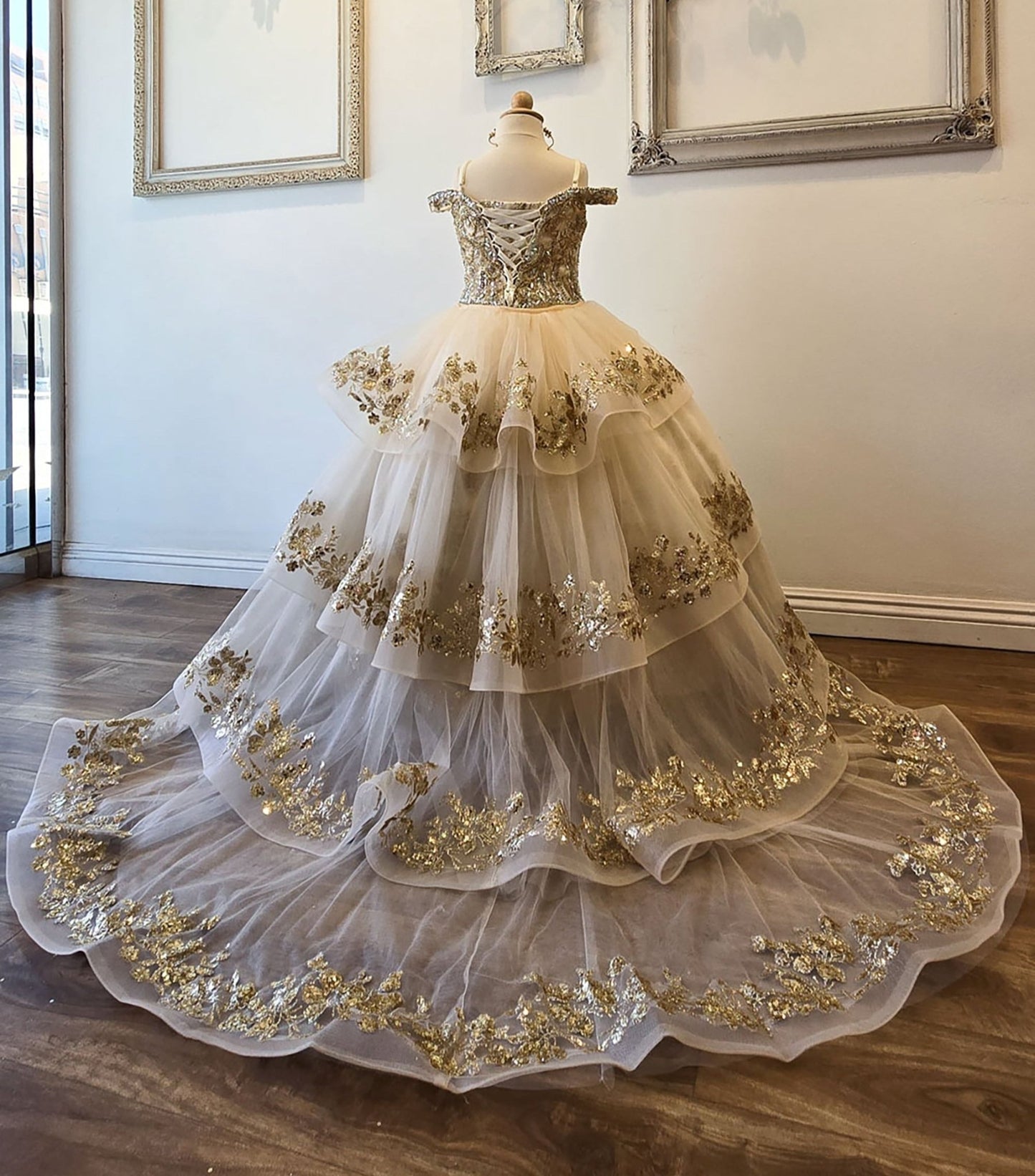 Back view of an ivory champagne kids mini quinceanera mini quince dress with lace-up corset, oversized bow, glitter tulle skirt, and detachable long train.