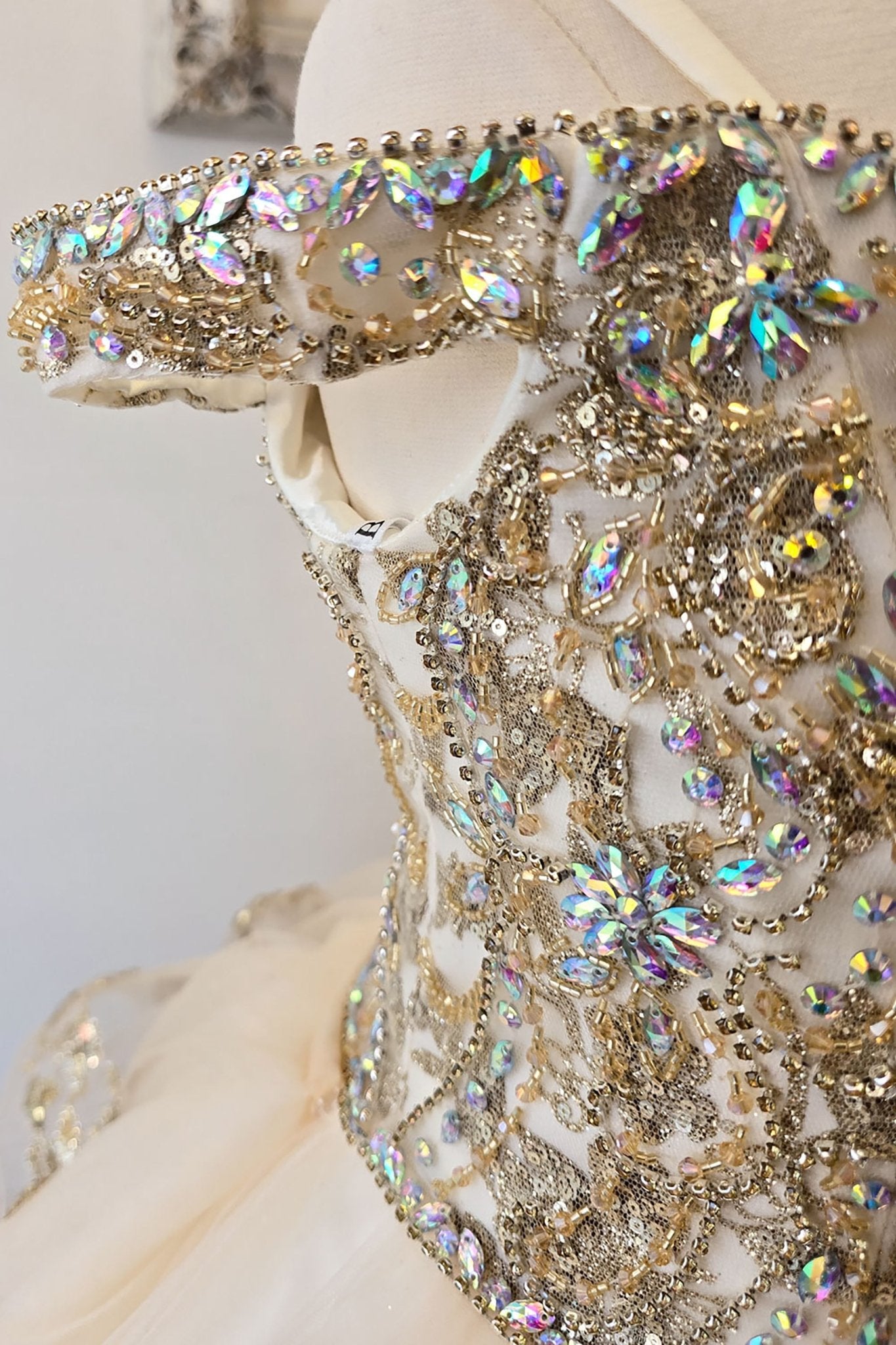 Side close-up of an ivory champagne kids mini quinceanera mini quince dress showing gem-embellished bodice, puffed sleeve detail, and glitter tulle fabric.