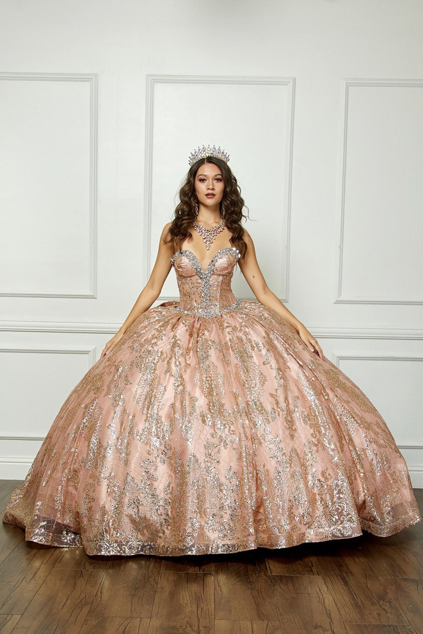 Woman in a sparkling gold quinceanera ball gown against a white paneled wall.