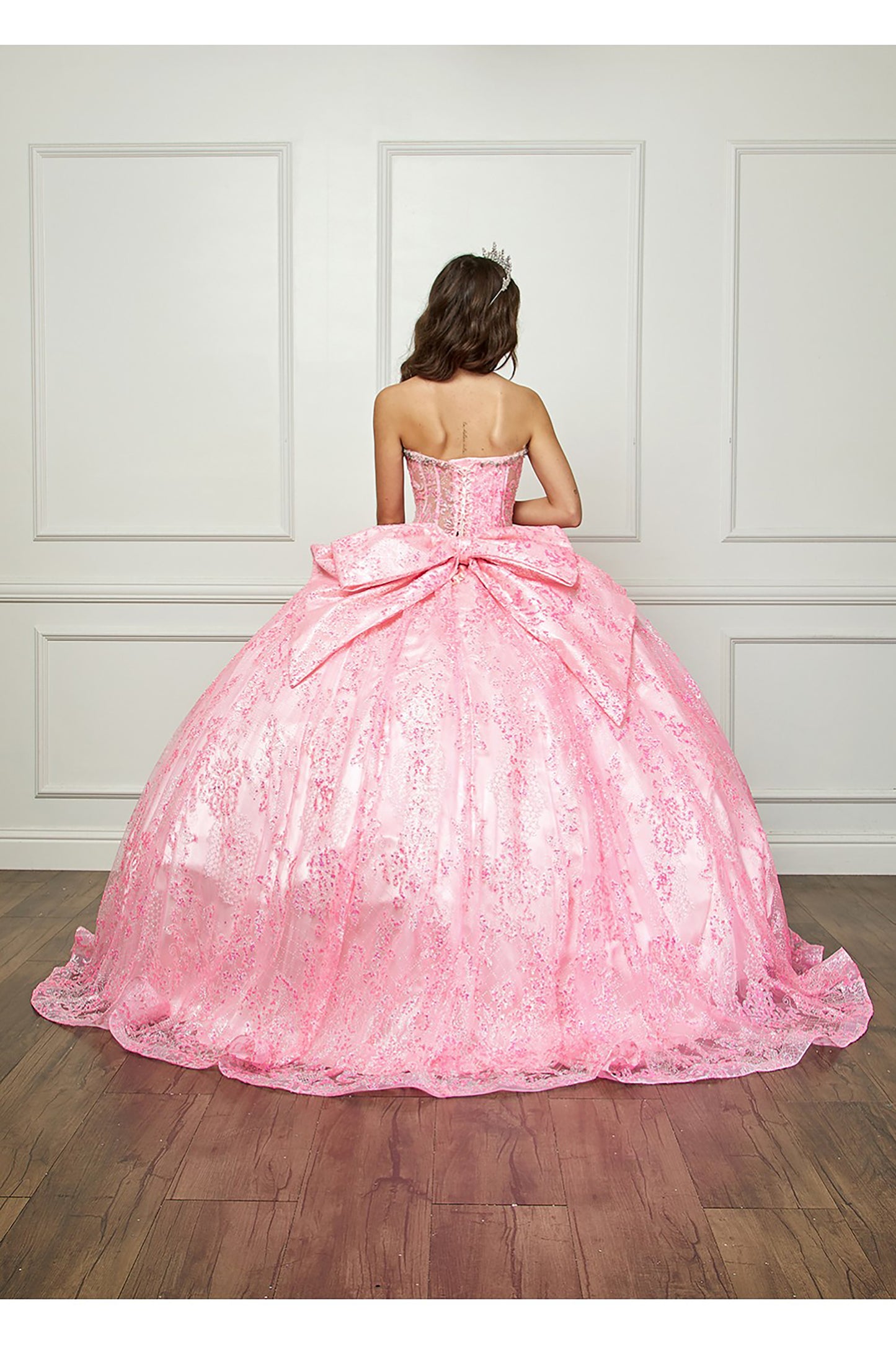 Pink Quinceanera | Spackly Sequins and Embellishments See-through Corset Bodice adorned with Shimmering Gems Quince Ballgown - back view of woman wearing dress with crown and big bow