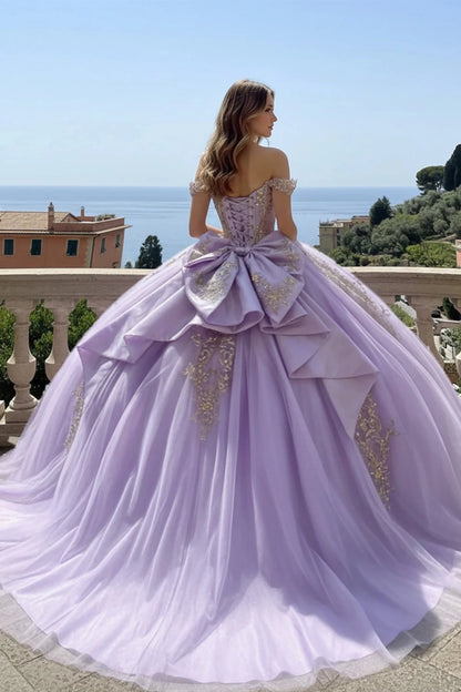 Lavender ball gown with a large bow and gold accents in an outdoor setting.