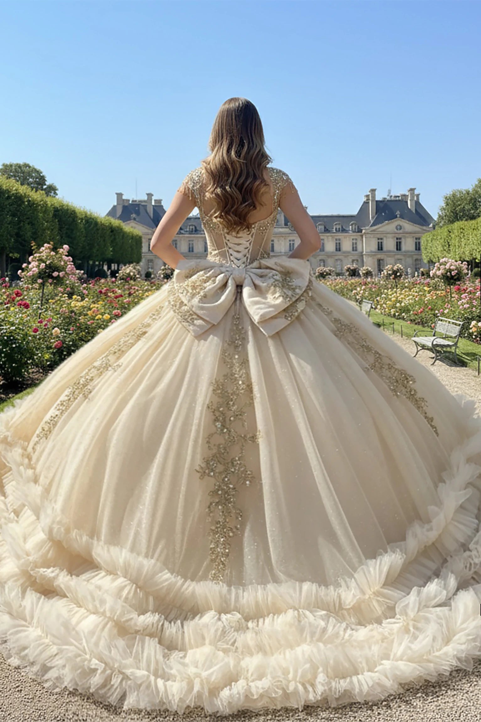 Woman in a champagne quince ball gown showing her back of the dress with large bow and long train 
