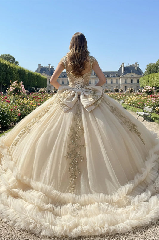 Woman in a champagne quince ball gown showing her back of the dress with large bow and long train