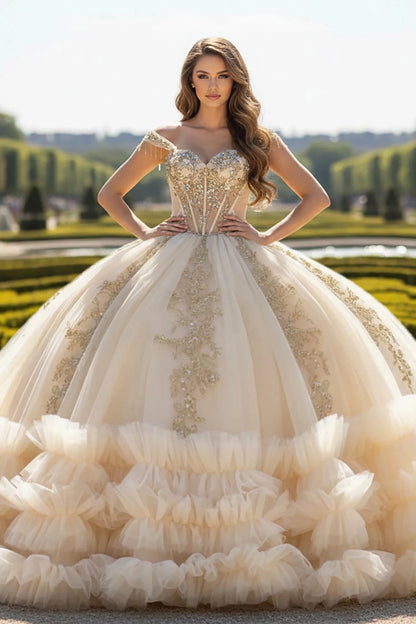 Woman in a luxurious champagne and gold embroidery ball gown with full layered tulle skirt standing in an outdoor setting with greenery.