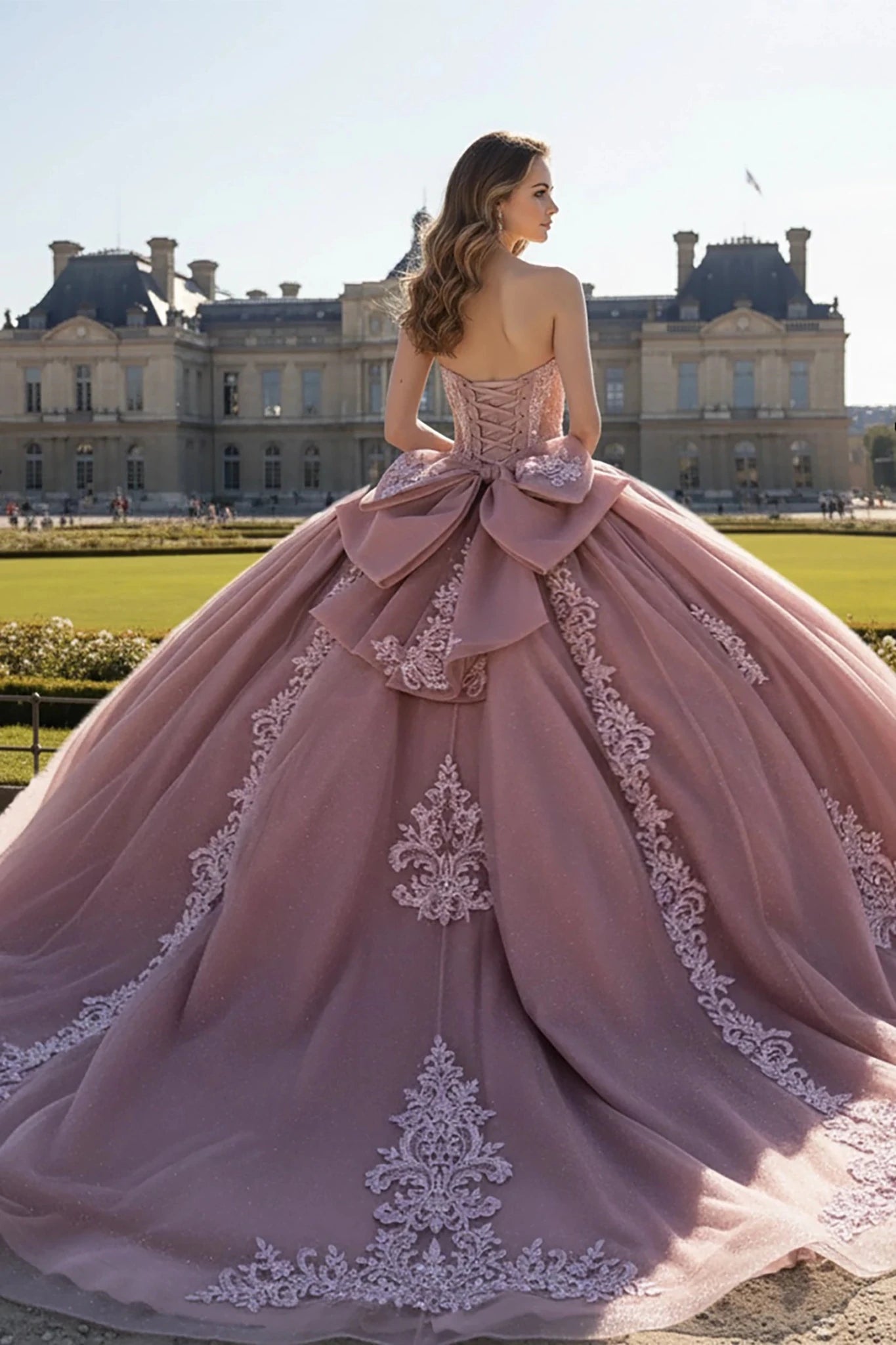 Woman in a rose color quince ball gown with large bow and embroidery  details standing in front of a historic building.