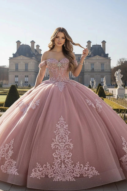 Woman in a rose ball gown with intricate embroidery standing in front of a classical building.