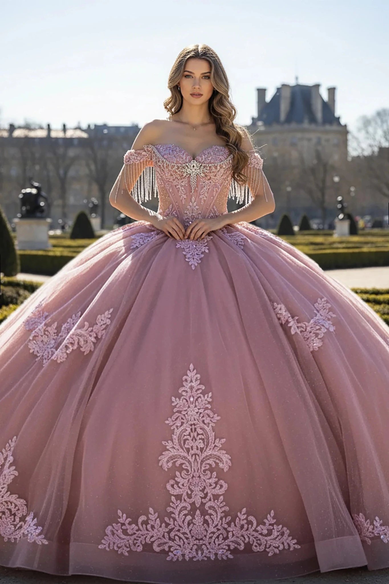 Woman wearing a rose, off-shoulder gown adorned with ornate lace appliqués that flow gracefully from the bodice down to the hem.