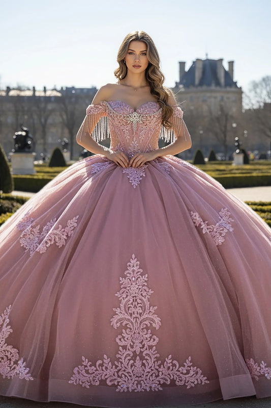 Woman wearing a rose, off-shoulder gown adorned with ornate lace appliqués that flow gracefully from the bodice down to the hem.