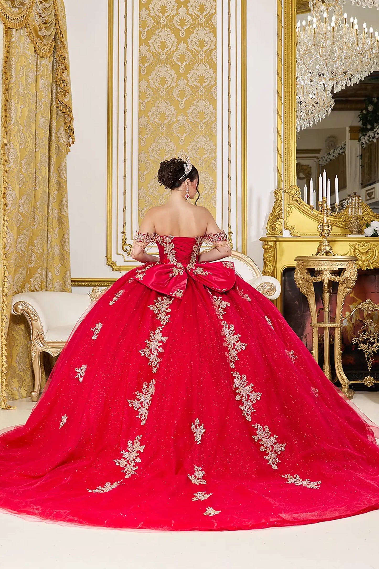 Woman back-facing in red off-shoulder sweetheart quinceañera dress with lace-up corset bodice, gold embroidery, and cascading full tulle skirt
