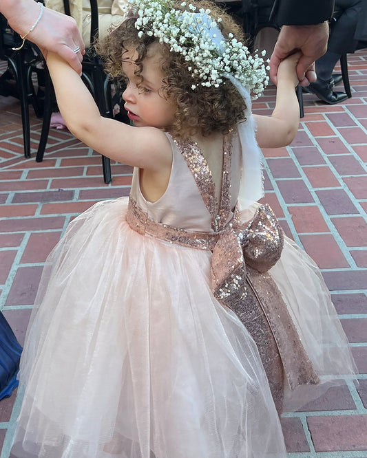 Young girl in a pink dress with a bow, standing on a brick pavement.
