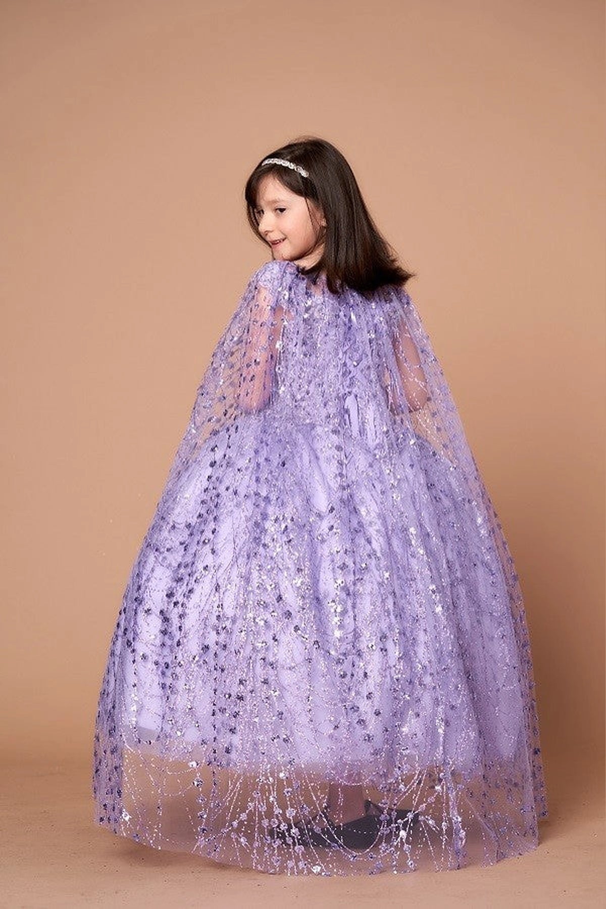 A graceful front view, the Lilac mini quince dress showcases off-the-shoulder bodice with allover sequins and glitter and matching cape over a full sparkling skirt.