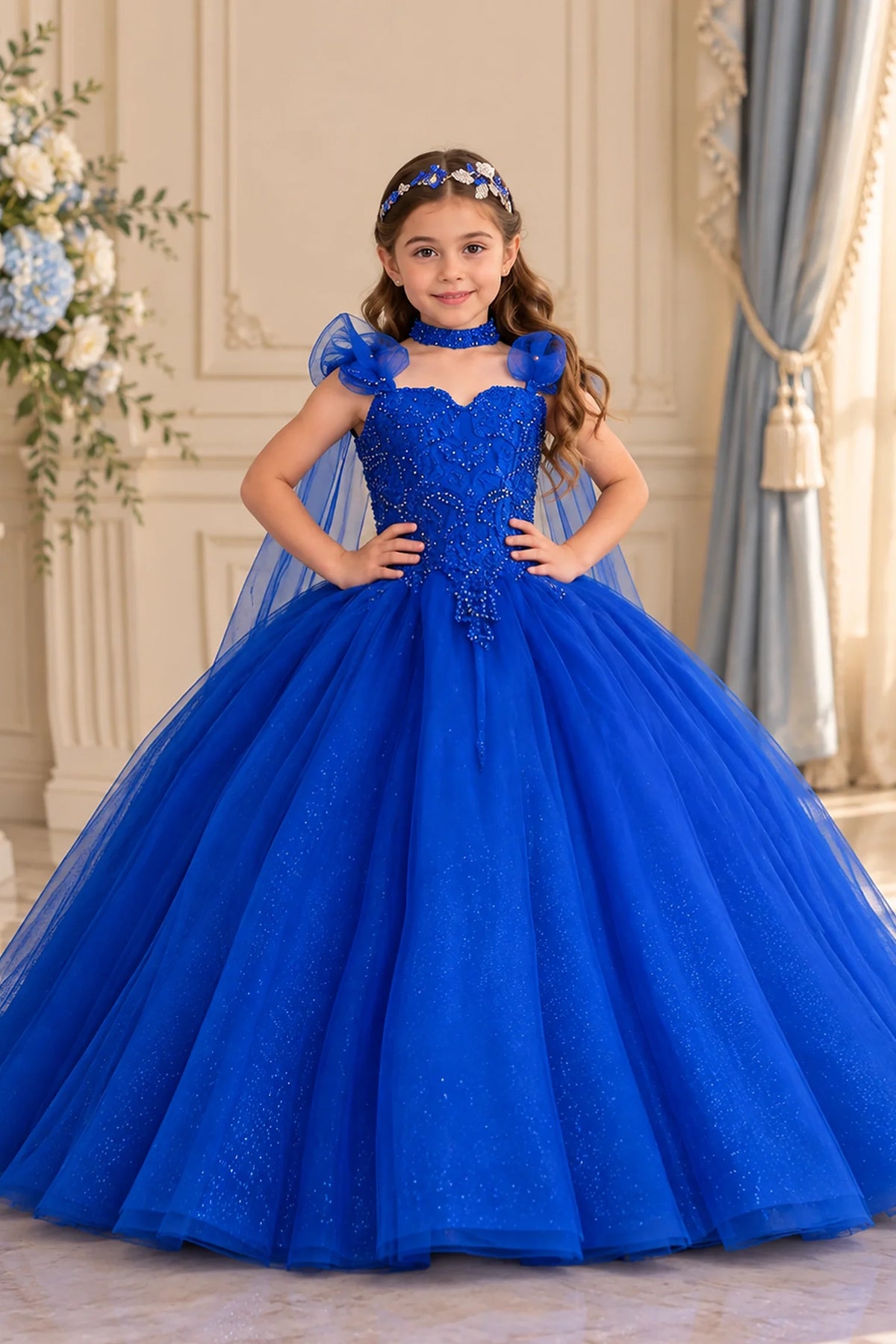 At the bodice and skirt, the Royal Blue mini quince dress showcases removable sheer shoulder cape and glittering embroidered tulle ball gown skirt.