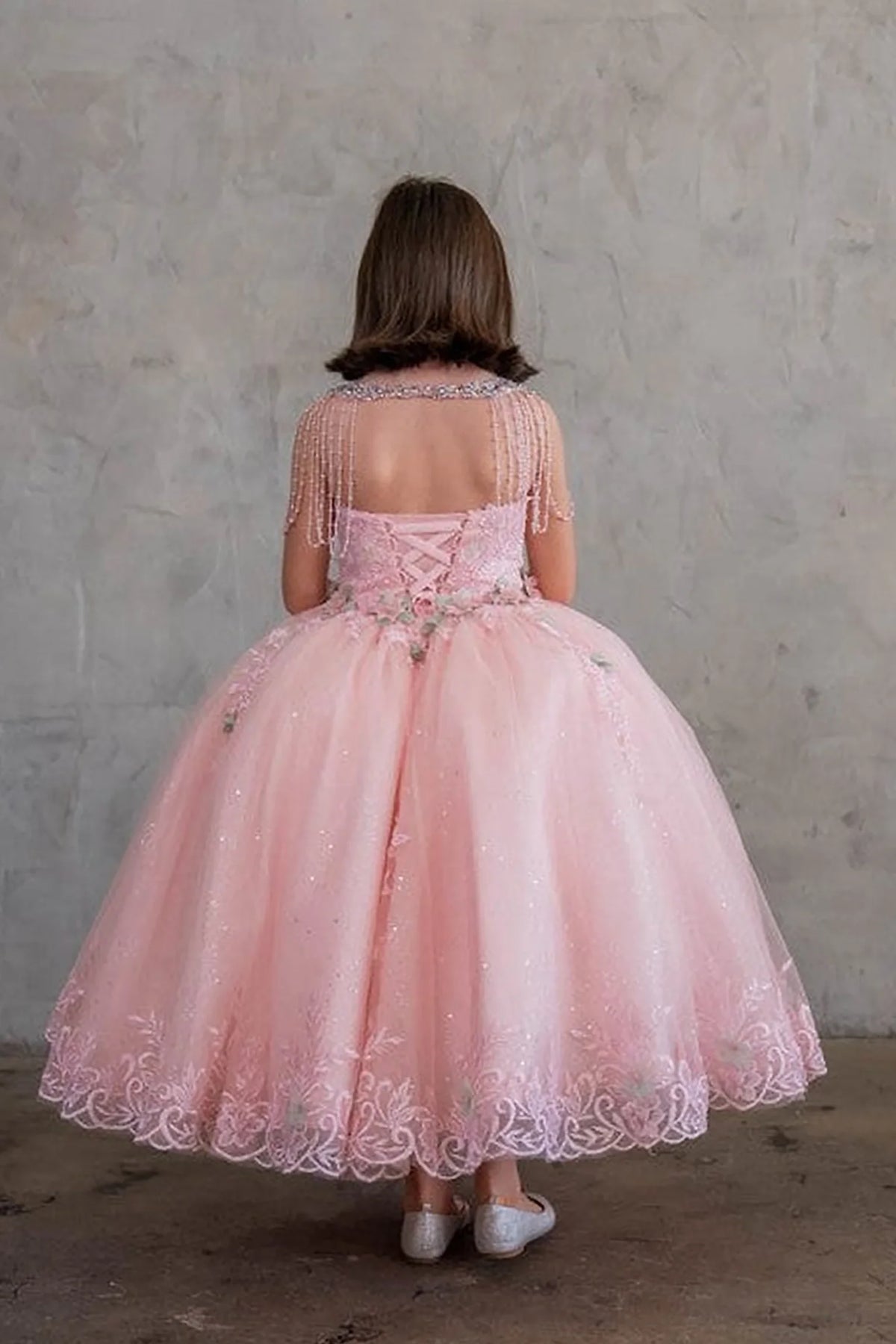 The reverse view reveals, the Blush Pink mini quince dress displays its lace-up finish and full tulle skirt with embroidered lace trim.