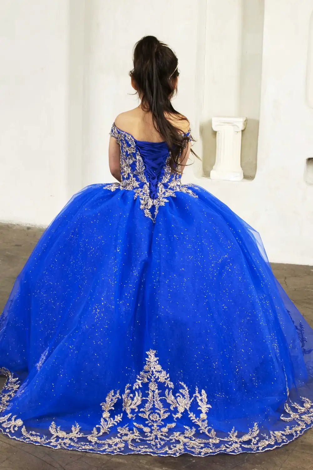 Back view of royal blue mini quince dress with lace-up closure, lace appliqué accents, glitter tulle, and cascading layered skirt.
