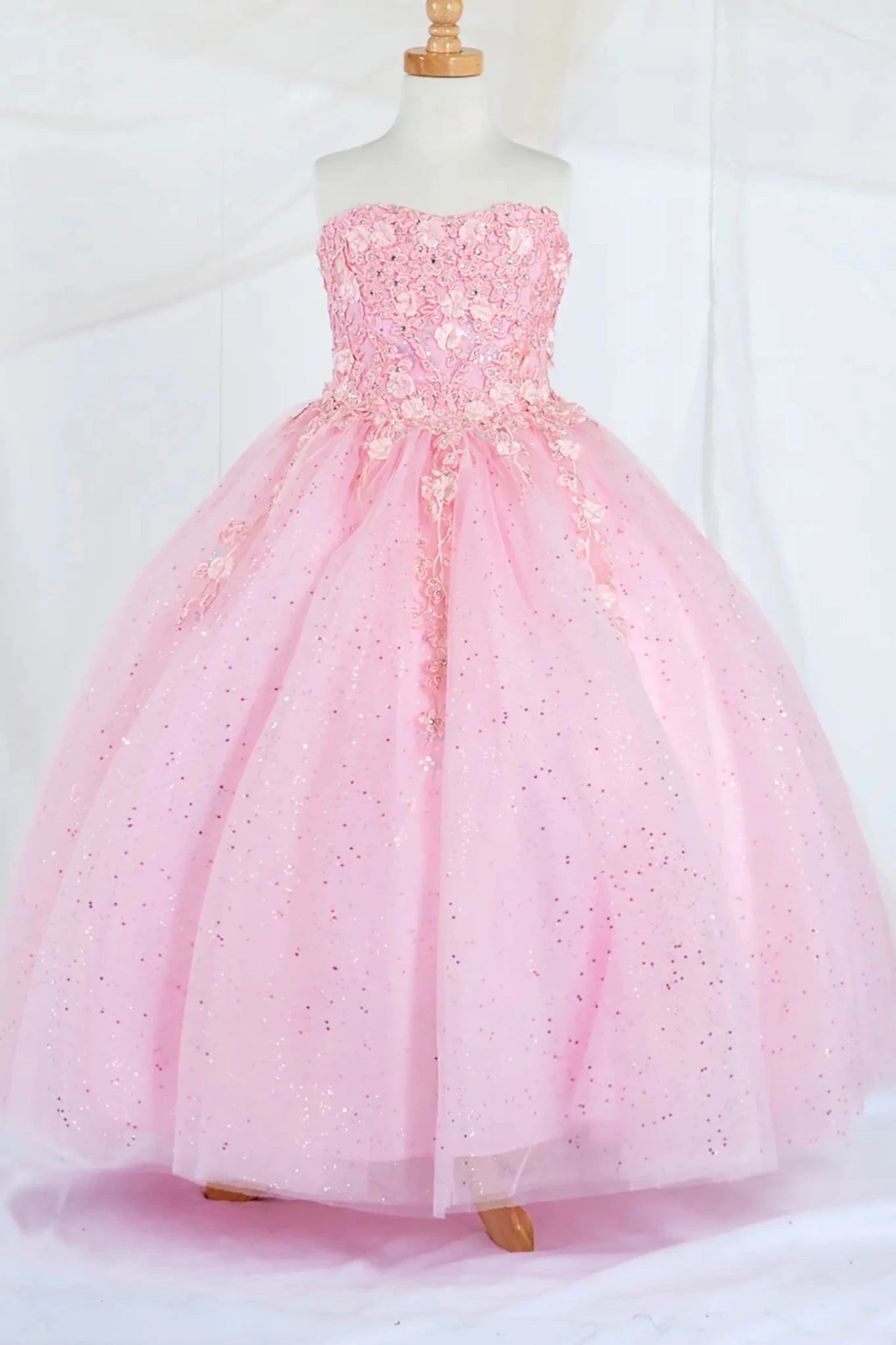 Front-facing display of a bubble-pink mini quince dress featuring a strapless 3D floral appliqué bodice and a full glitter tulle layered skirt.