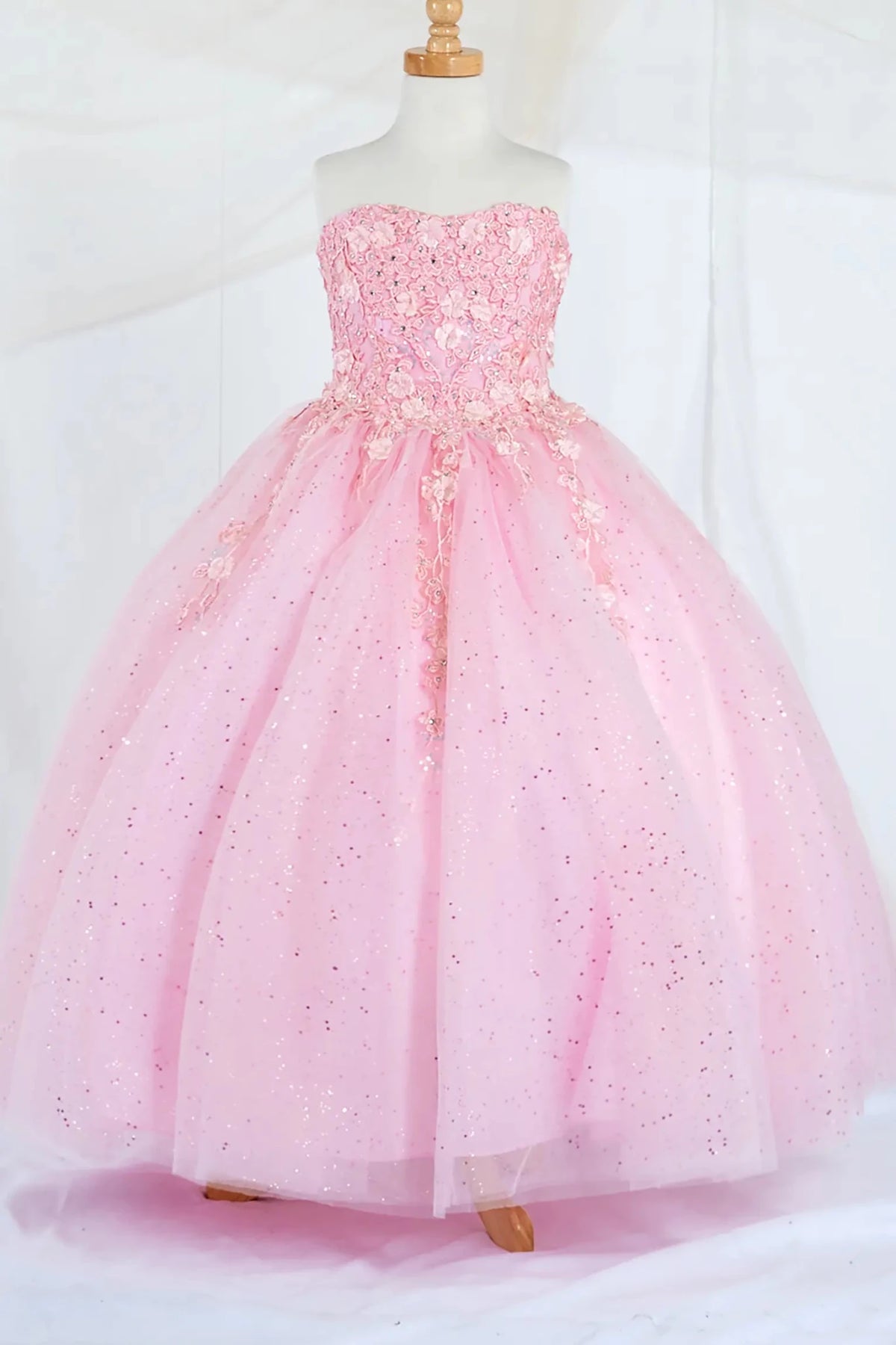 Front-facing display of a bubble-pink mini quince dress featuring a strapless 3D floral appliqué bodice and a full glitter tulle layered skirt.