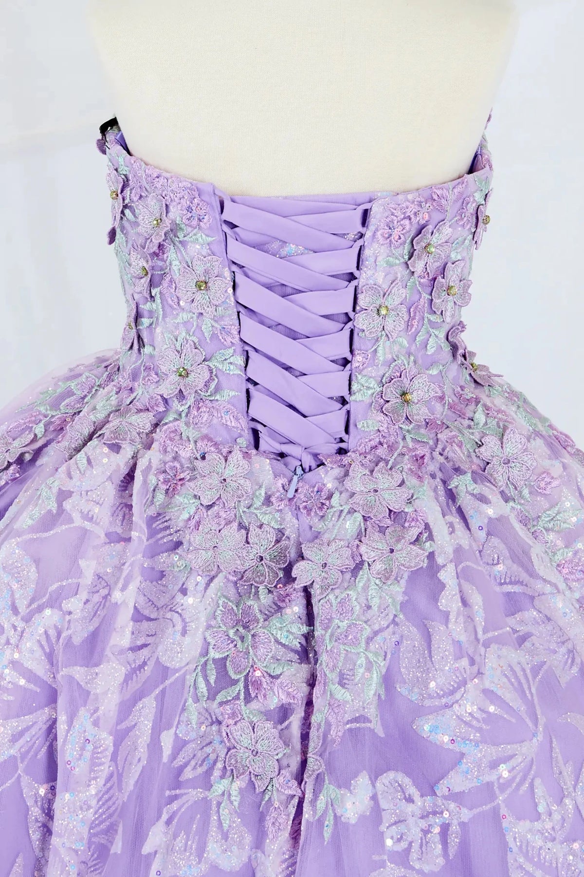 Close-up display highlighting the intricate 3D flower appliqué and delicate butterfly details on the bodice. Mini quince dress.