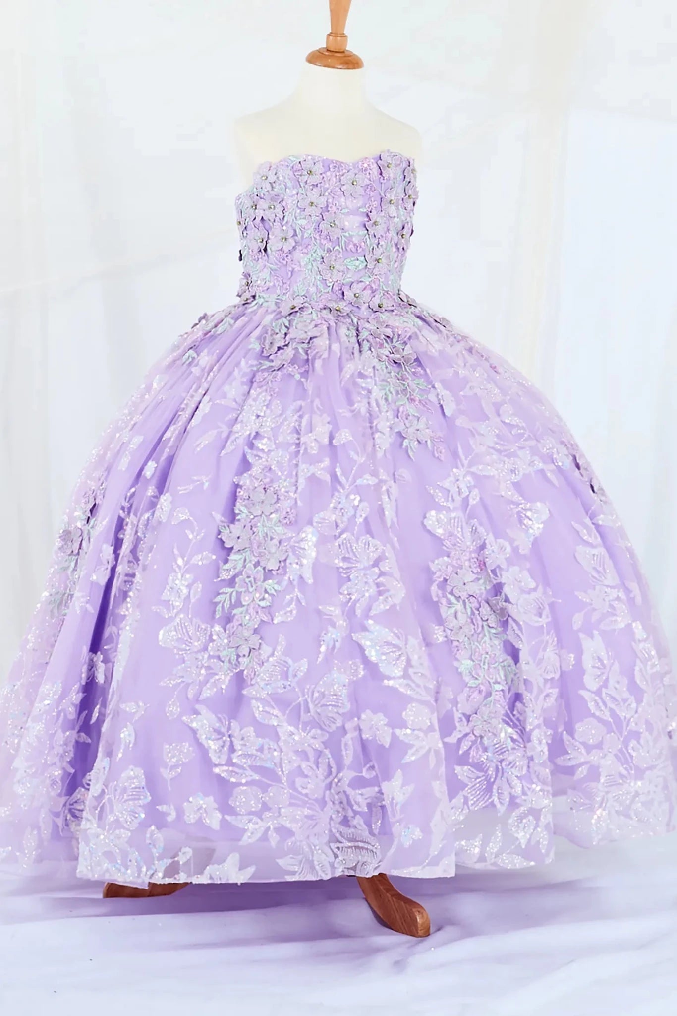 Side-facing display of a lilac mini quince dress featuring a 3D floral appliqué bodice with butterfly accents and a glitter tulle layered skirt.