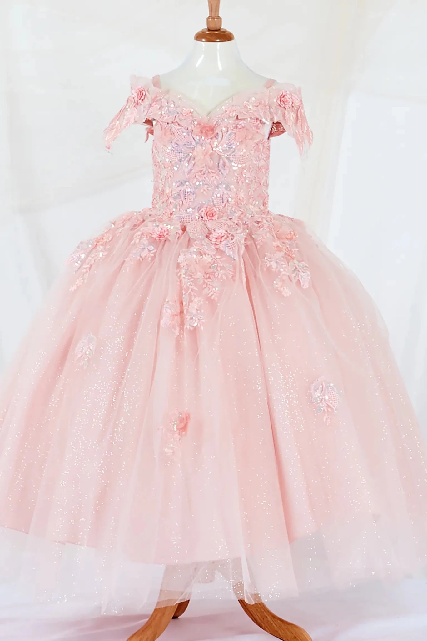 Front-facing display of an elegant blush mini quince dress featuring a fitted bodice, detachable bow accent, and a glitter tulle layered skirt.