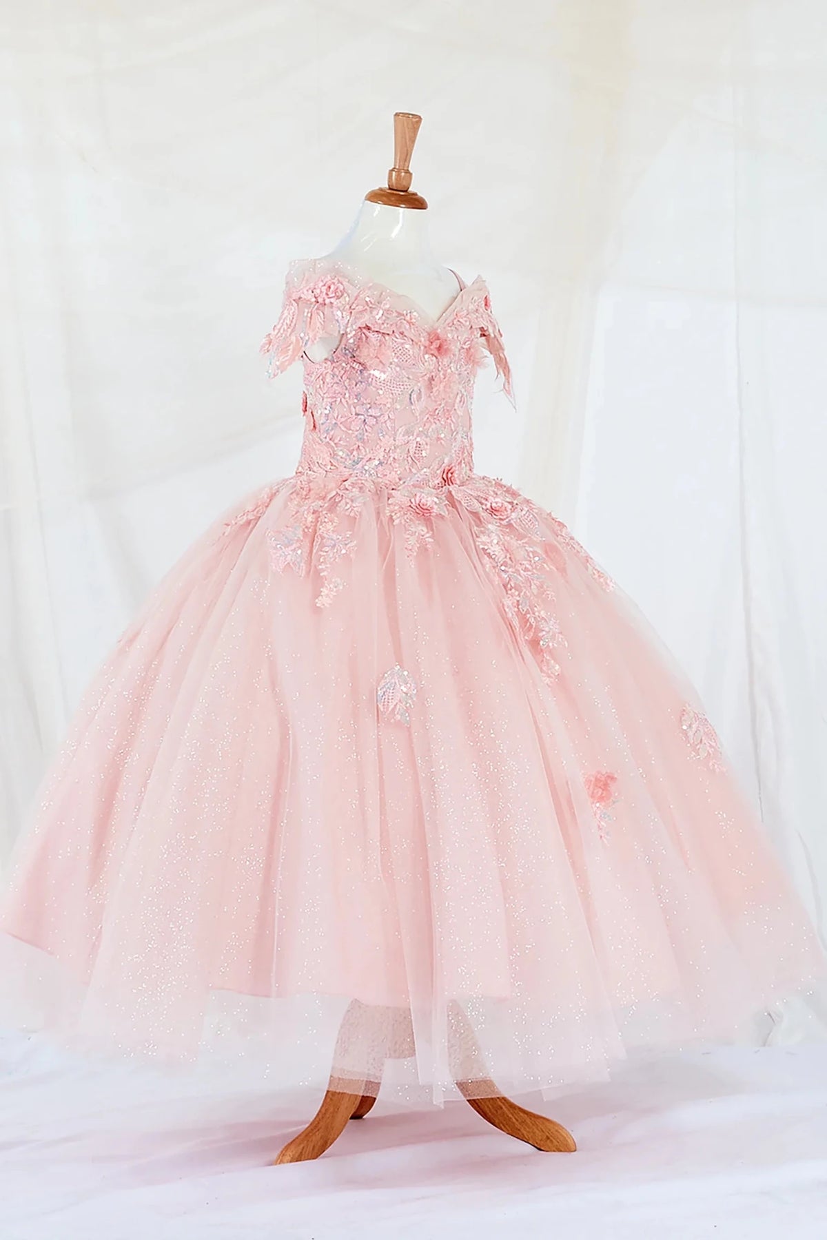 Side-facing display of an elegant blush mini quince dress featuring a fitted bodice, detachable bow accent, and a glitter tulle layered skirt.