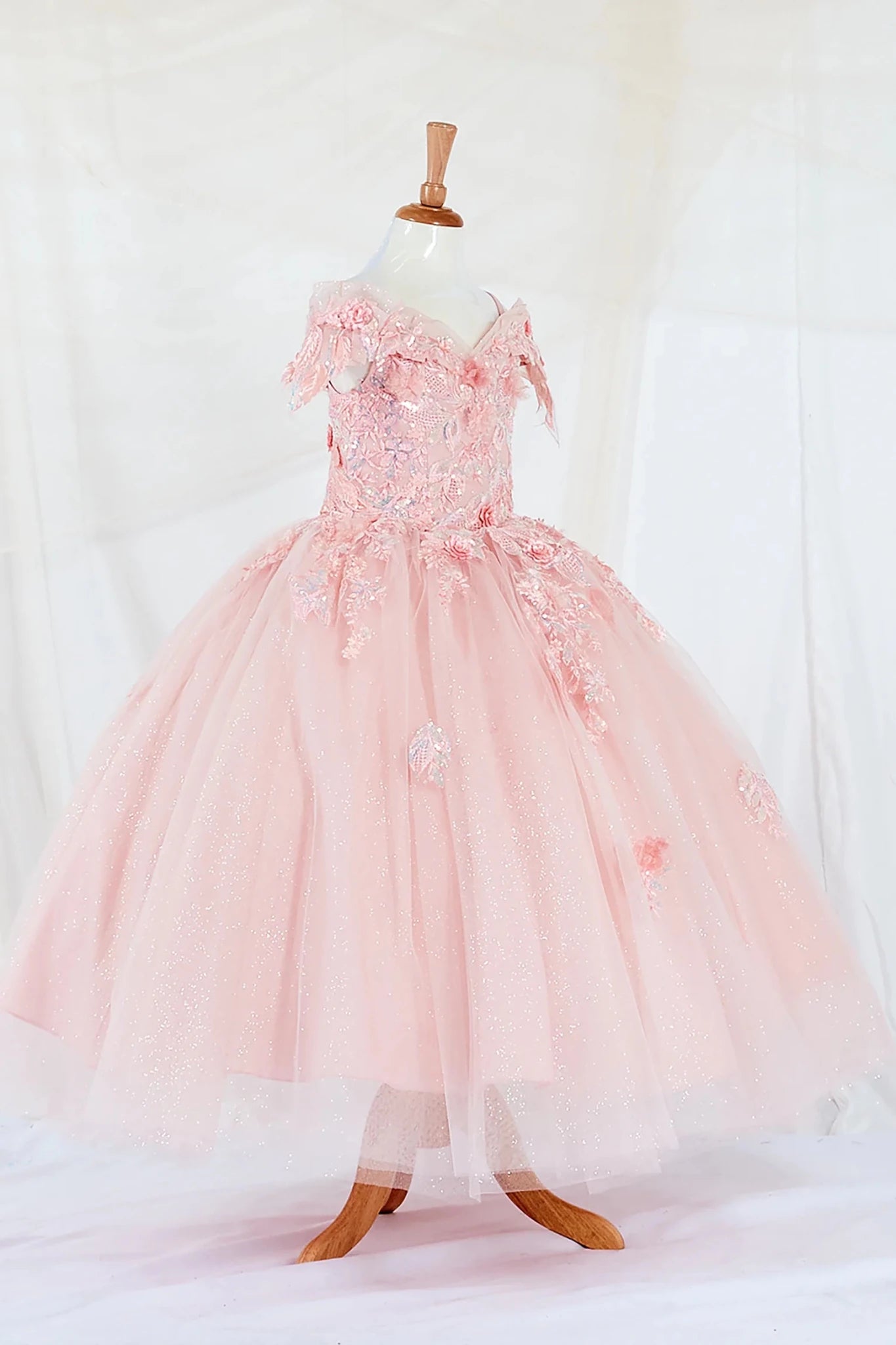 Side-facing display of an elegant blush mini quince dress featuring a fitted bodice, detachable bow accent, and a glitter tulle layered skirt.
