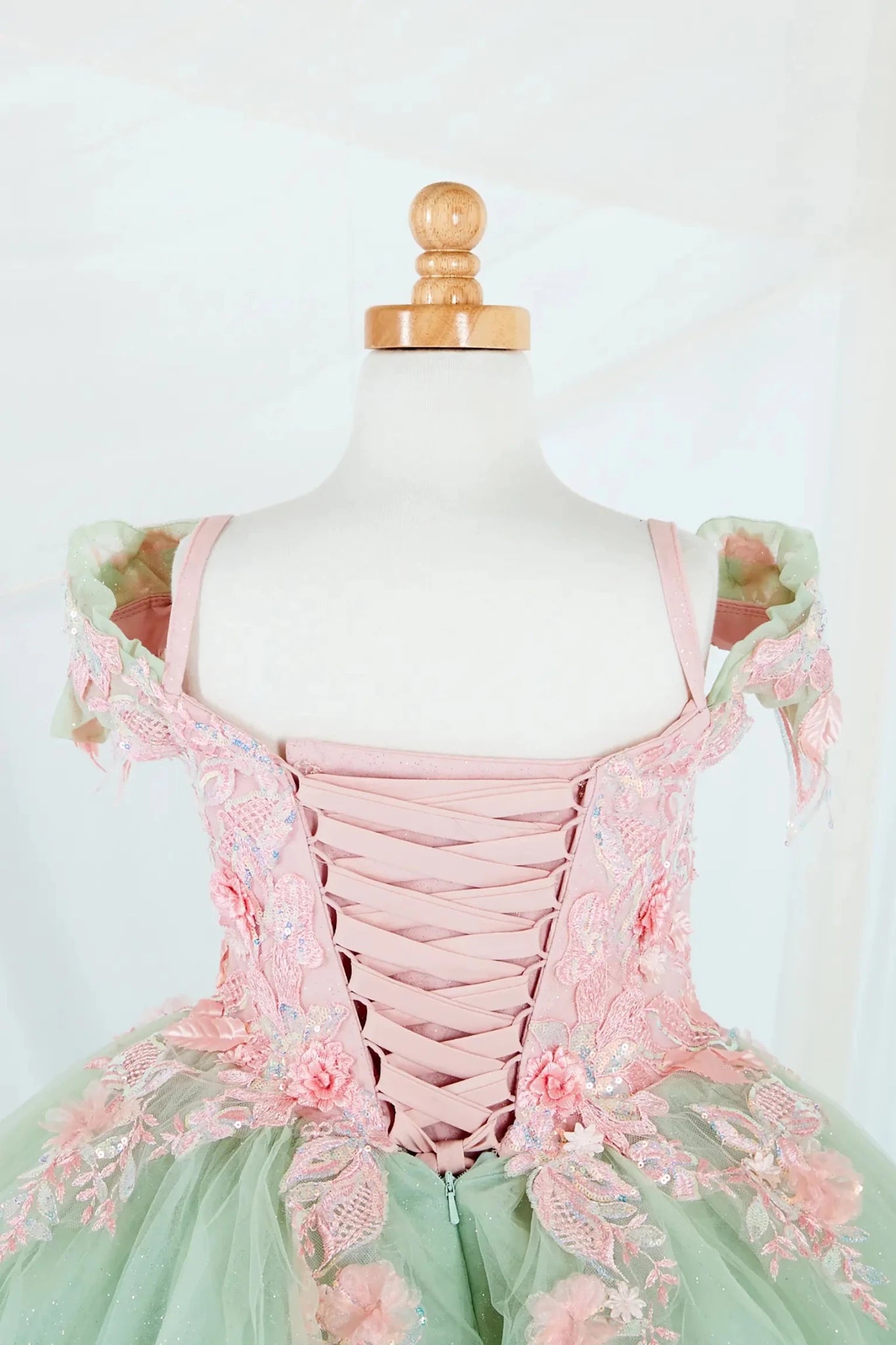 Close-up display highlighting the fitted bodice, detachable bow accent, and the shimmer of the glitter tulle layers. Mini quince dress.