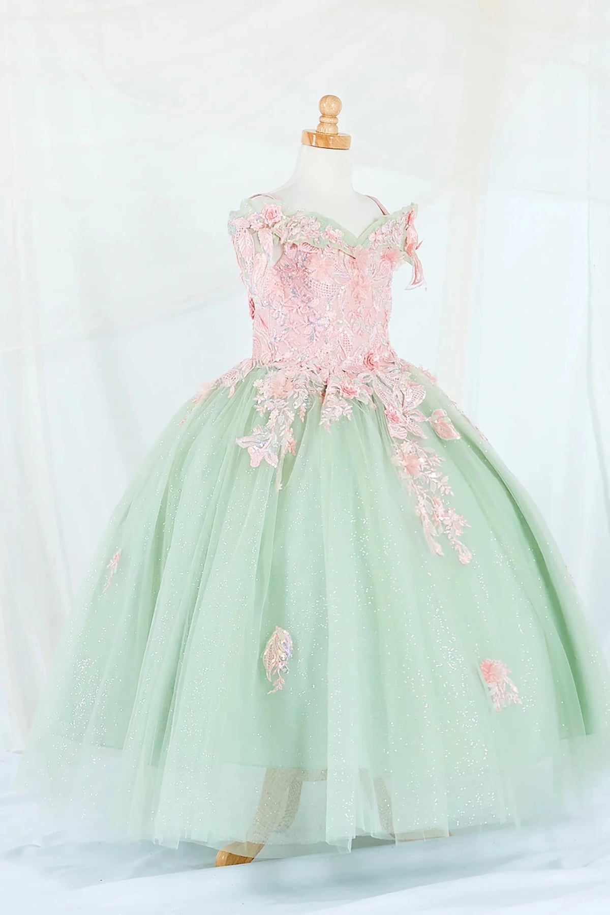 Side-facing display of an elegant sage and blush mini quince dress featuring a fitted bodice, detachable bow accent, and a glitter tulle layered skirt.