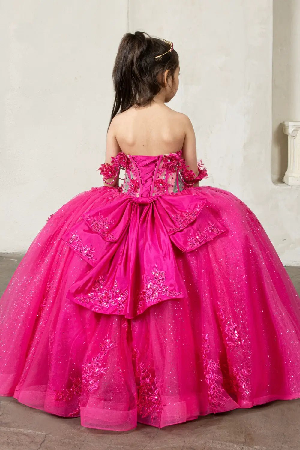 A fuchsia mini quince dress with floral details and large back bow.