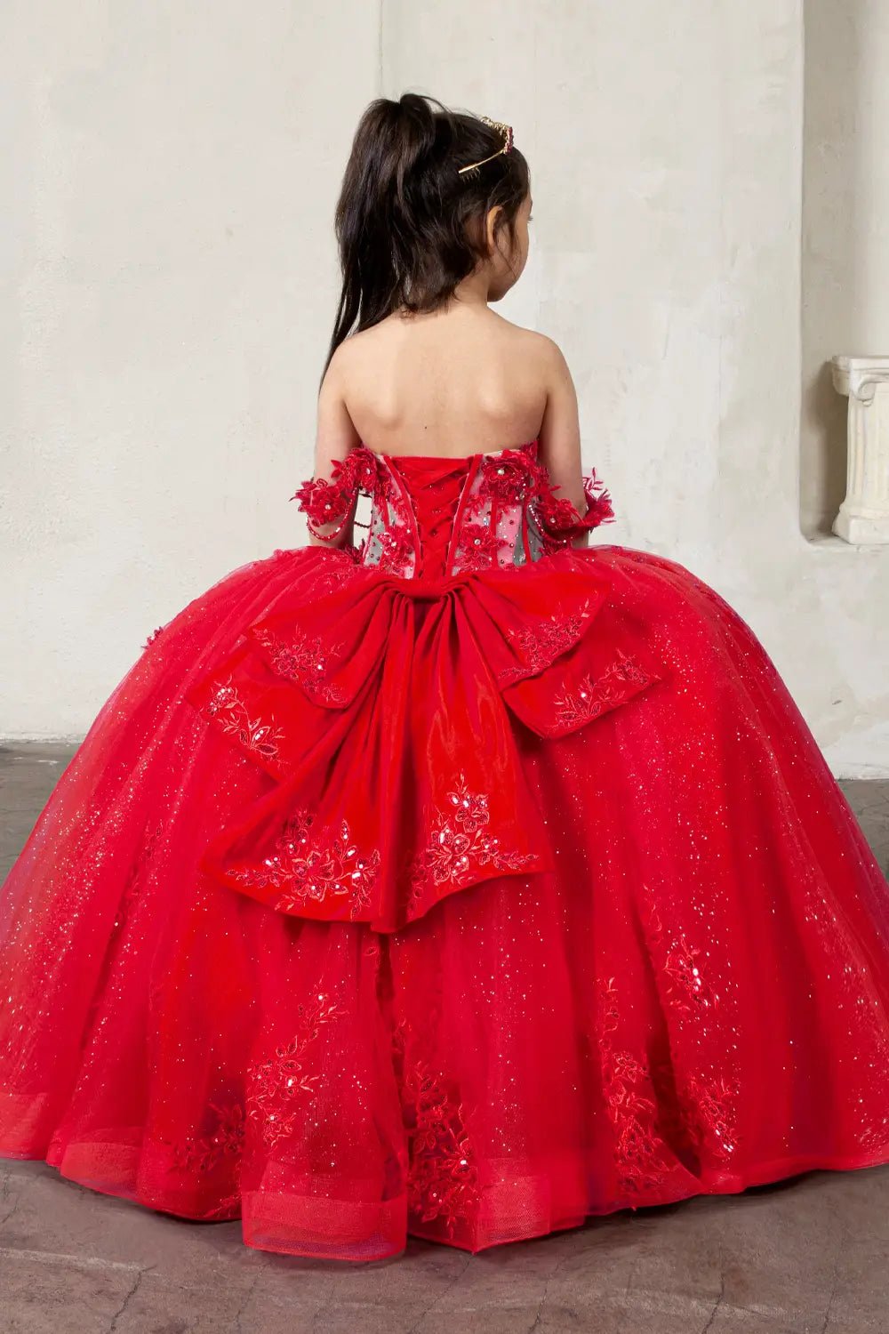 Back view of red mini quince dress with lace-up closure, detachable bow accent, crystal beading, and cascading glitter tulle skirt.