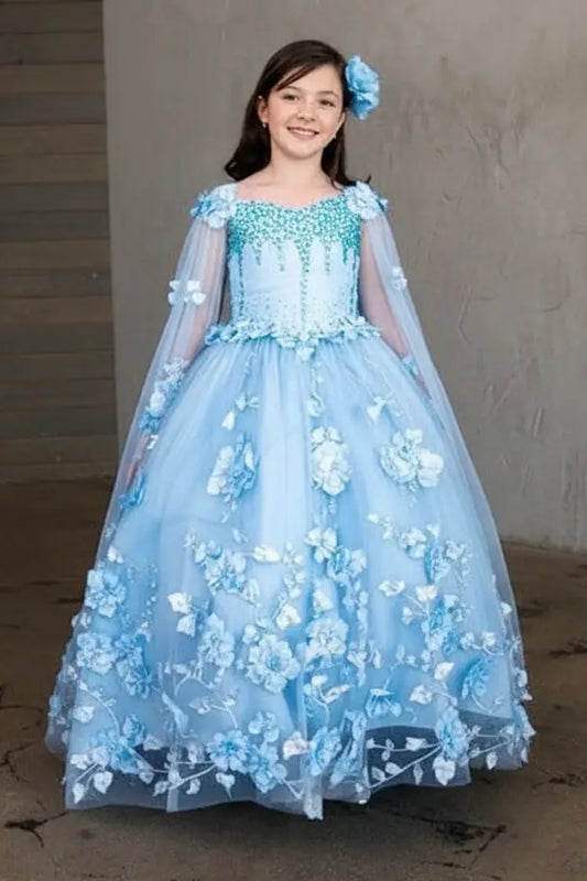 Young woman standing front-facing in elegant light blue ball gown with two-tone tail, matching cape, and voluminous skirt
