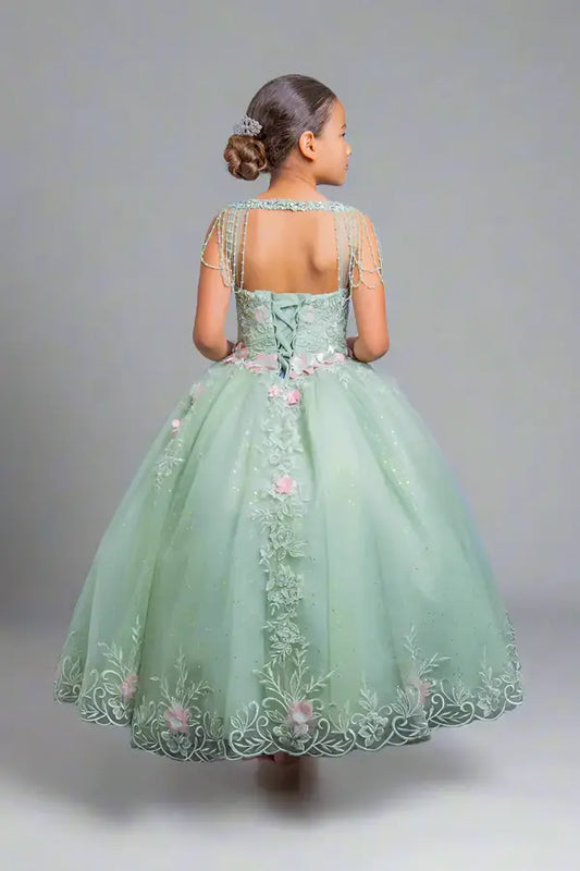 Young woman standing back-facing in sage ball gown with lace-up closure, beaded fringe accents, 3D floral appliqués, and cascading layered skirt

