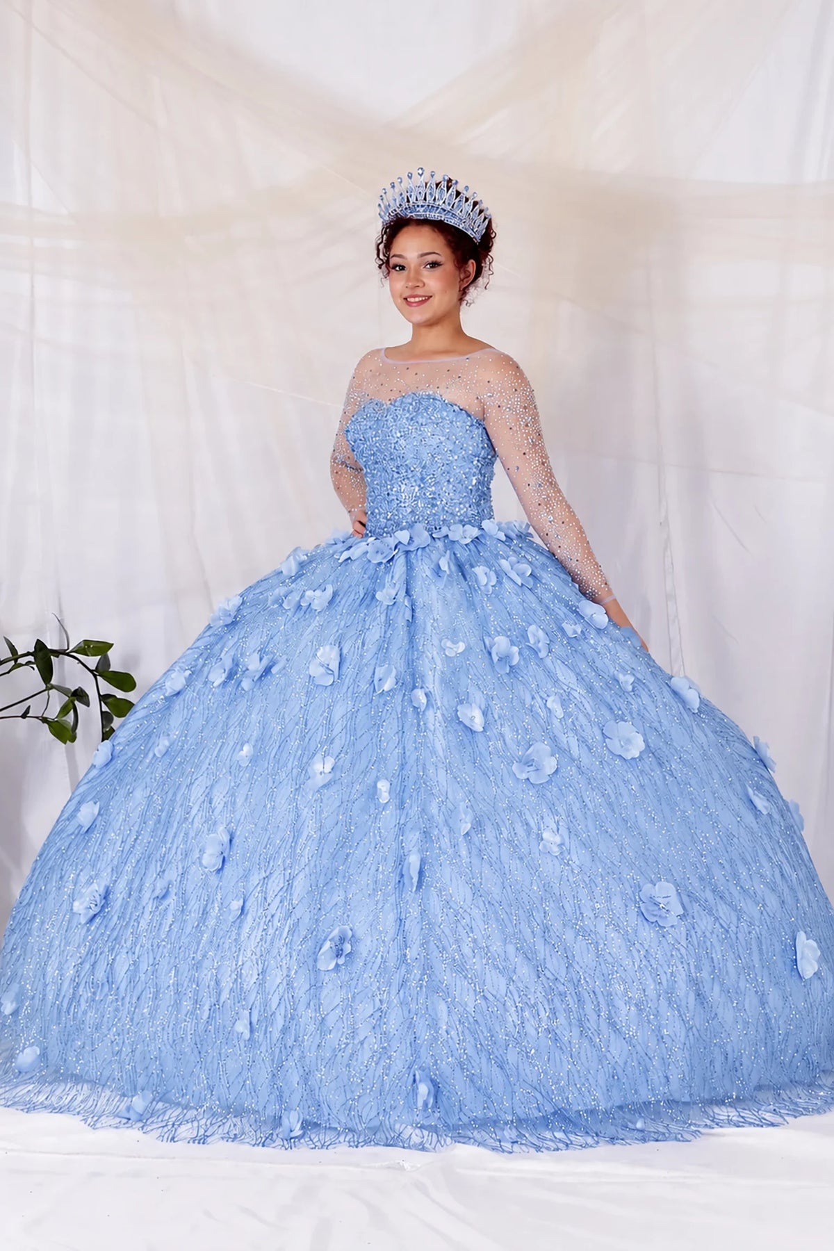 Dusty Blue quinceañera dress showcases dimensional flowers across the textured skirt above sheer long sleeves and a fitted corset bodice.