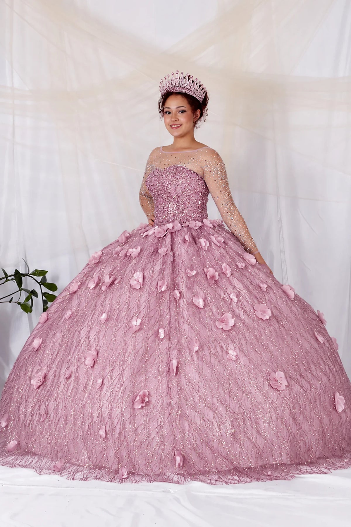 Dusty Rose quinceañera dress showcases dimensional flowers across the textured skirt above sheer long sleeves and a fitted corset bodice.