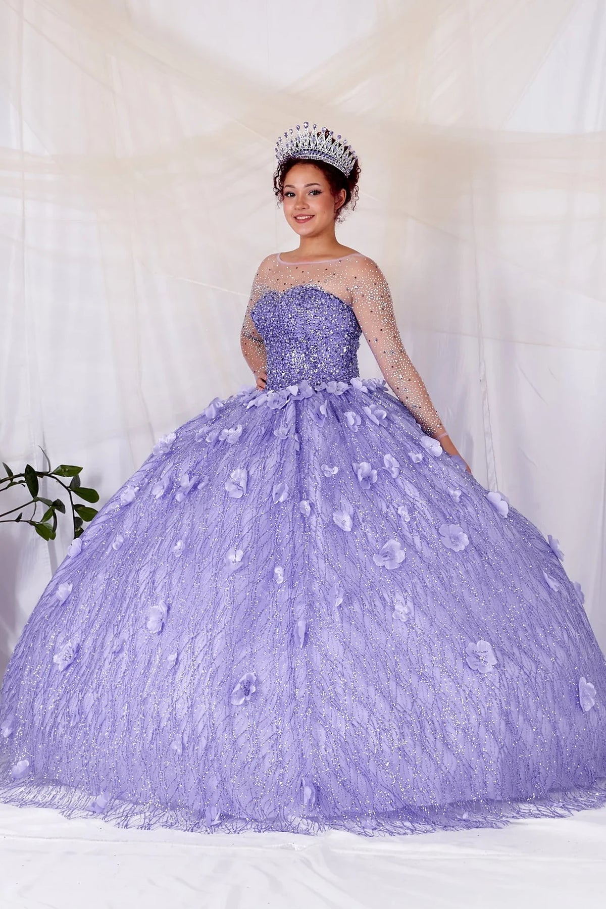 Lilac quinceañera dress showcases dimensional flowers across the textured skirt above sheer long sleeves and a fitted corset bodice.
