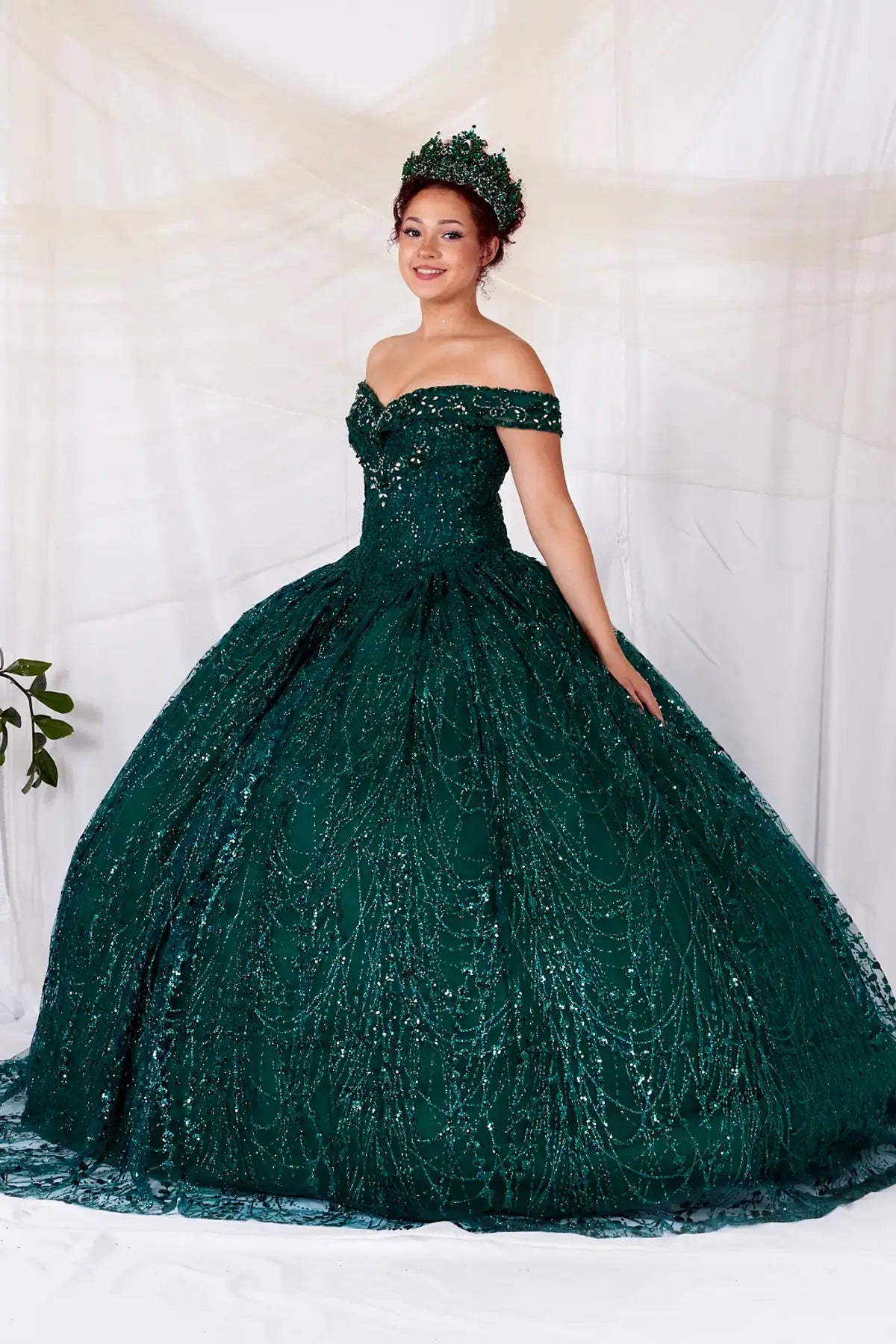 Side View of a woman wearing Rich green evening dress with shimmering sequins soft off-shoulder sleeves and fluid silhouette enhanced by cape