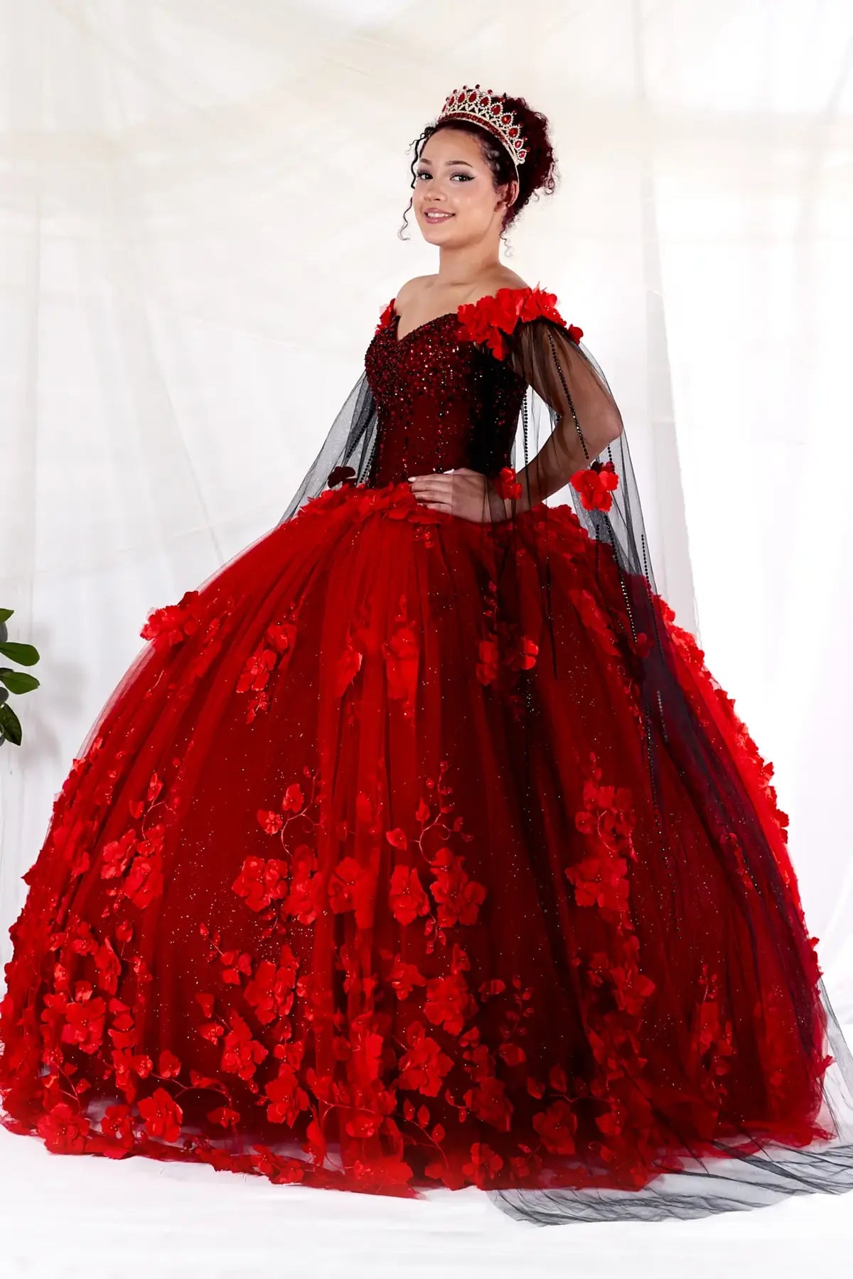 Side View of a woman wearing Bold red and black gown with floral accents structured bodice and flowing silhouette enhanced by cape
