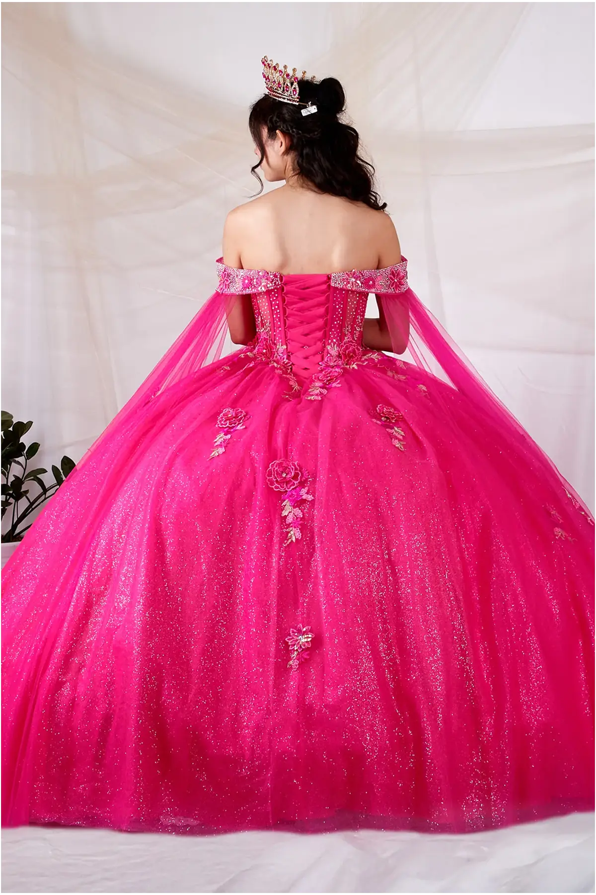 Back-Facing of a woman wearing Hot pink formal gown featuring structured back full skirt and detachable cape detail